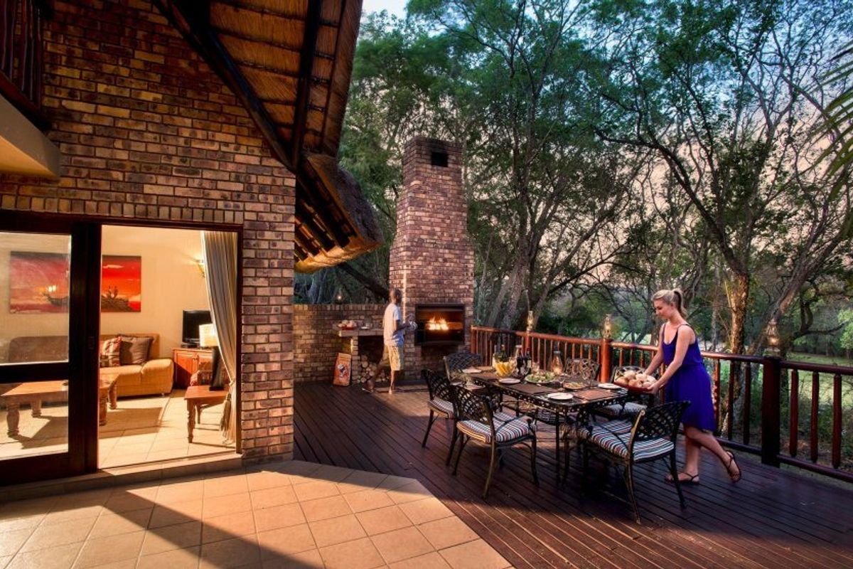 Spacious outdoor patio featuring a built-in brick fireplace, timber decking, and a thatched roof, offering a seamless transition to the surrounding natural landscape.
