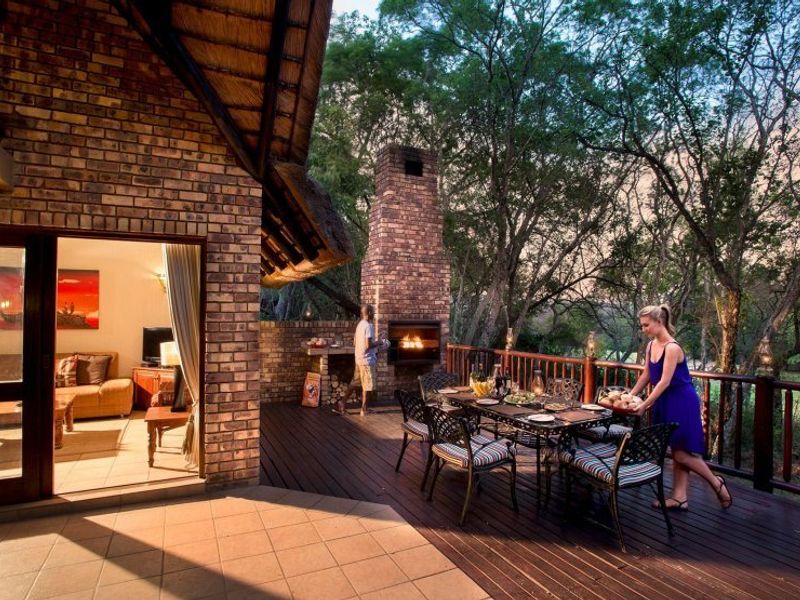 Spacious outdoor patio featuring a built-in brick fireplace, timber decking, and a thatched roof, offering a seamless transition to the surrounding natural landscape.