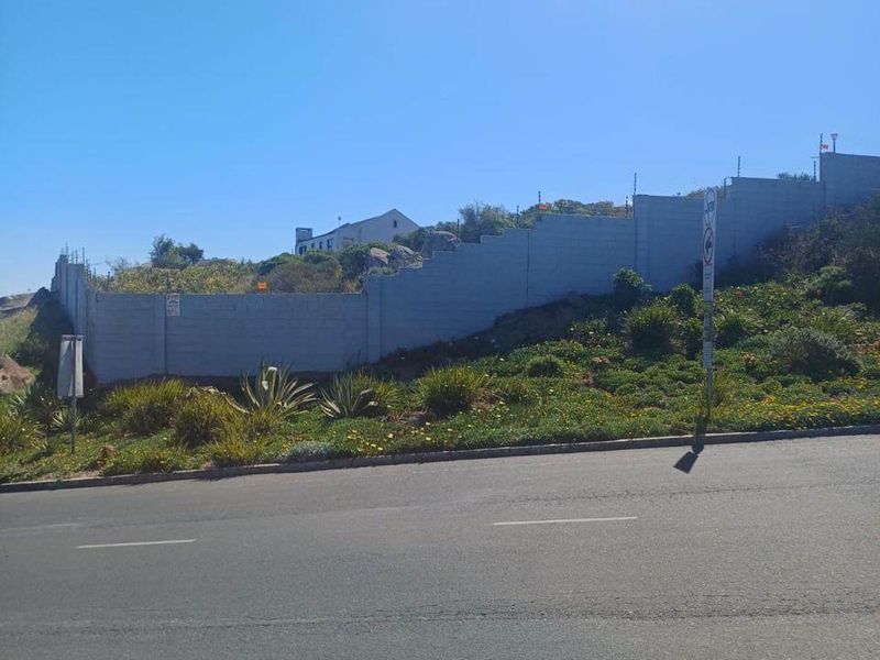 Street view of a vacant residential plot featuring a perimeter wall with electric fencing, situated along an asphalt road.