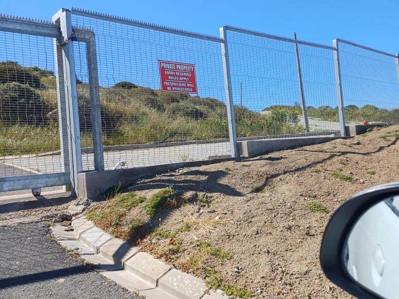 A view of the property boundary featuring secure wire mesh fencing, a concrete curb, and gated access from the street.