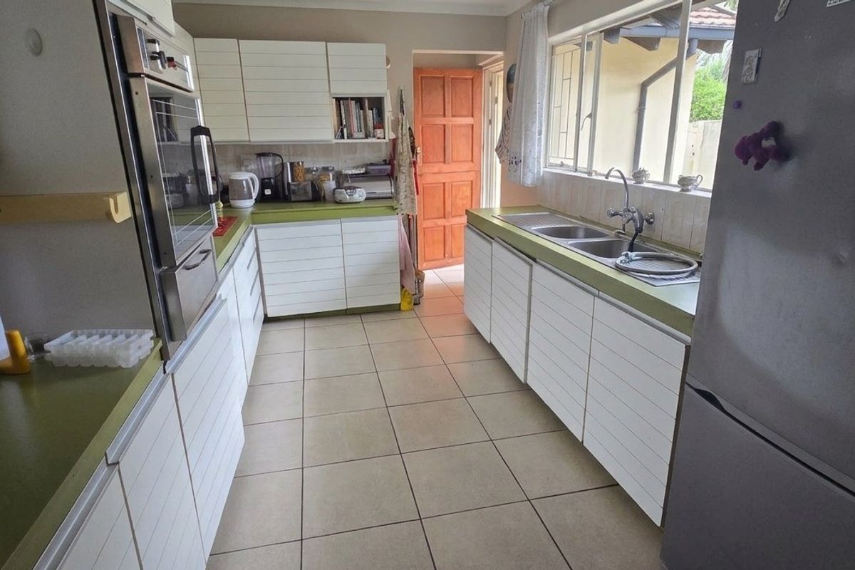 A functional kitchen featuring white cabinetry, green countertops, a built-in oven, and a double sink with tiled flooring throughout.