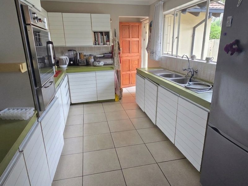 A functional kitchen featuring white cabinetry, green countertops, a built-in oven, and a double sink with tiled flooring throughout.