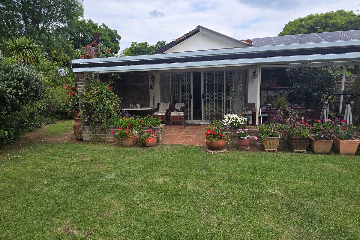 Rear view of the property featuring a covered patio area, brick paving, and established garden space with solar panels installed on the roof.