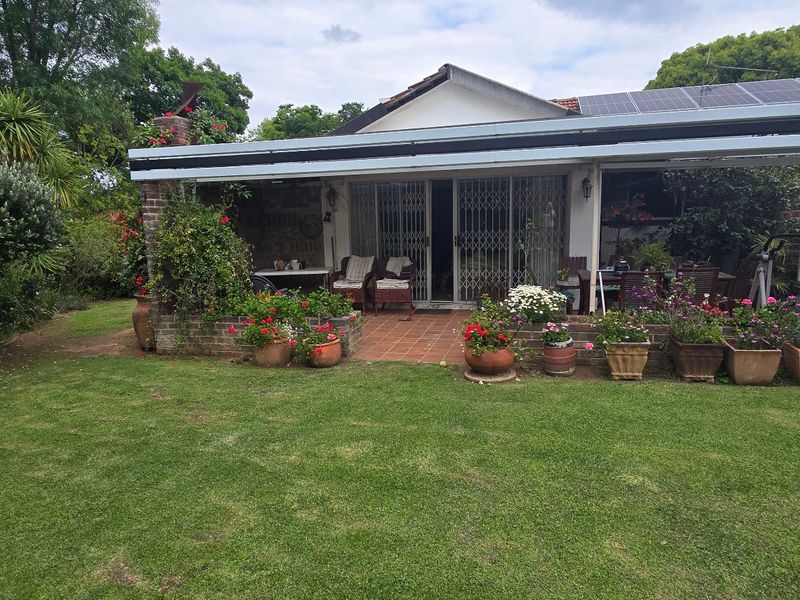 Rear view of the property featuring a covered patio area, brick paving, and established garden space with solar panels installed on the roof.