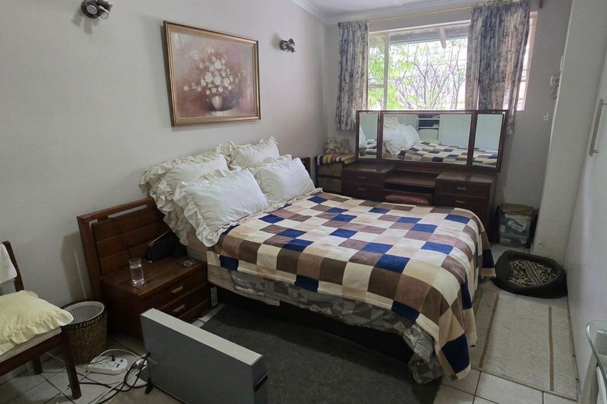 A functional bedroom featuring built-in cupboards, tiled flooring, and wall-mounted lighting, offering a neutral base for potential cosmetic updates.