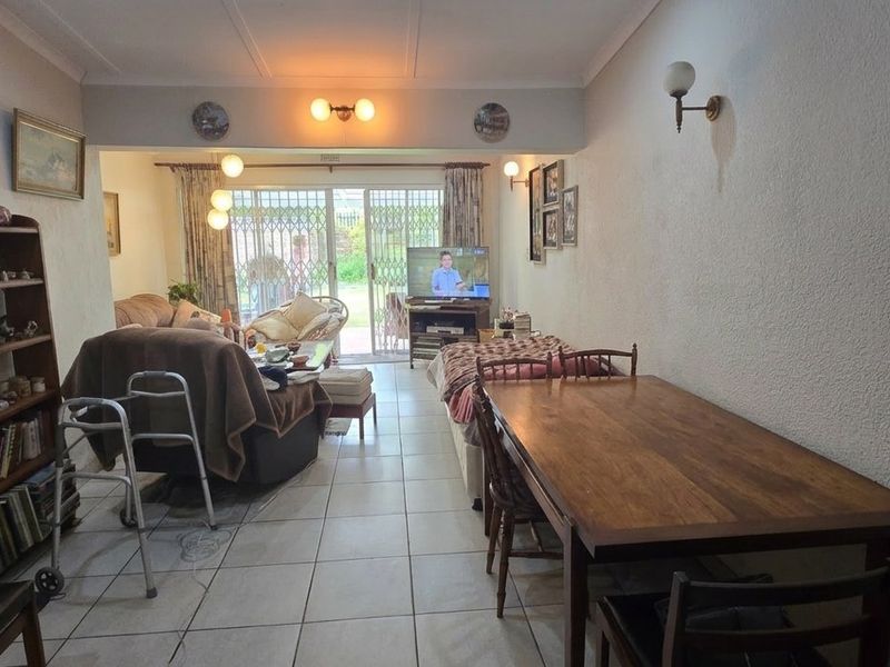 An open-plan living and dining area featuring tiled flooring, wall-mounted lighting, and sliding glass doors that provide access to the rear garden.
