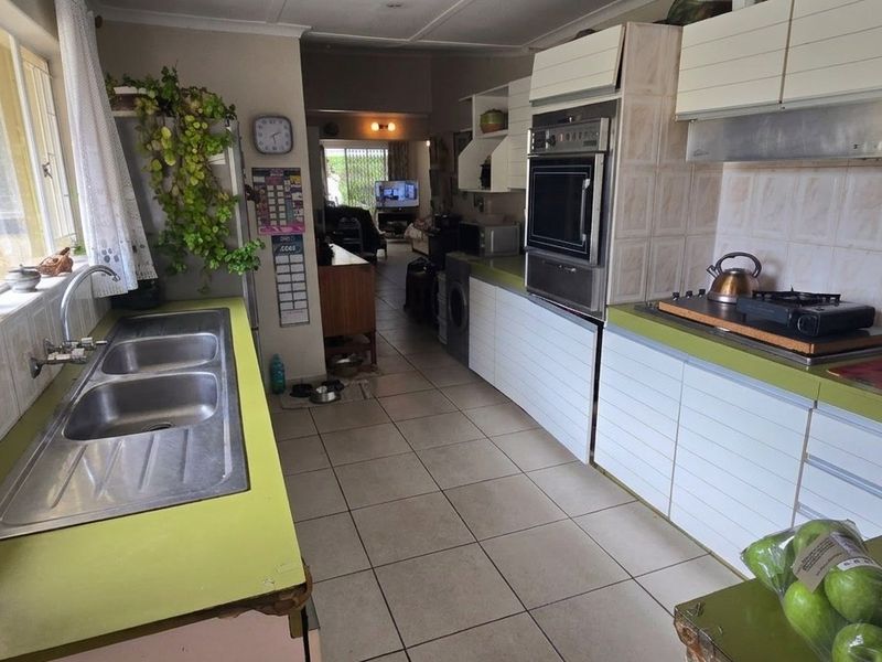 A functional kitchen featuring a double basin sink, built-in oven, extractor fan, and tiled finishes, offering potential for a modern renovation.