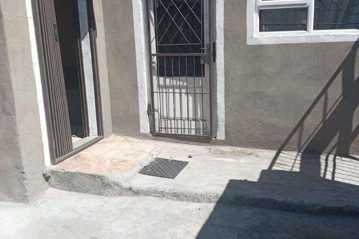 Rear exterior view of the property featuring a concrete patio area, security gate, and aluminium window frames.