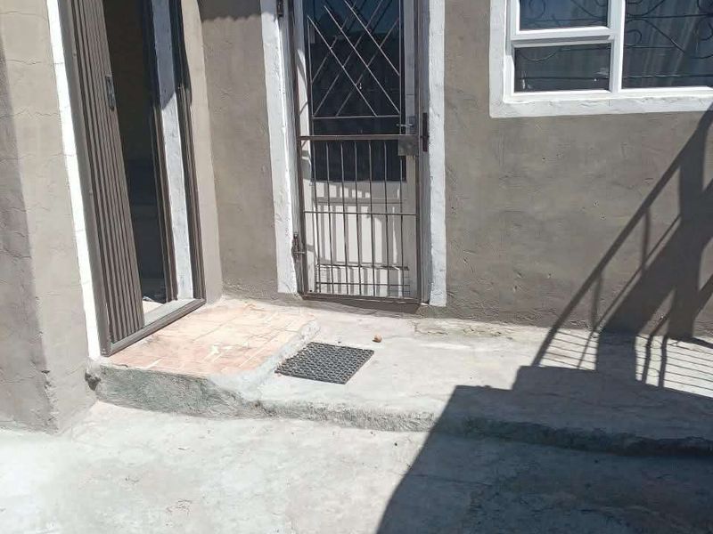 Rear exterior view of the property featuring a concrete patio area, security gate, and aluminium window frames.