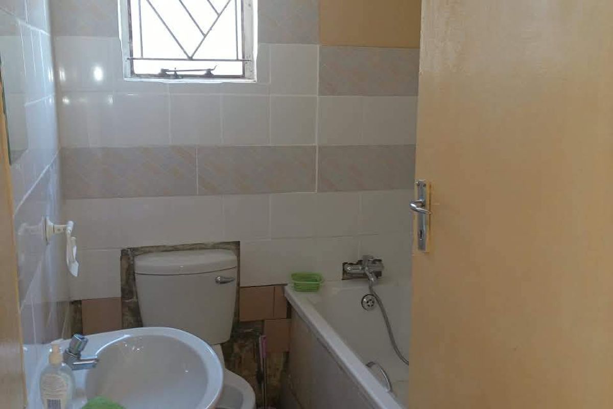 A compact bathroom featuring a pedestal basin, toilet, and bathtub with tiled finishes, currently requiring maintenance and cosmetic updates to the walls and flooring.