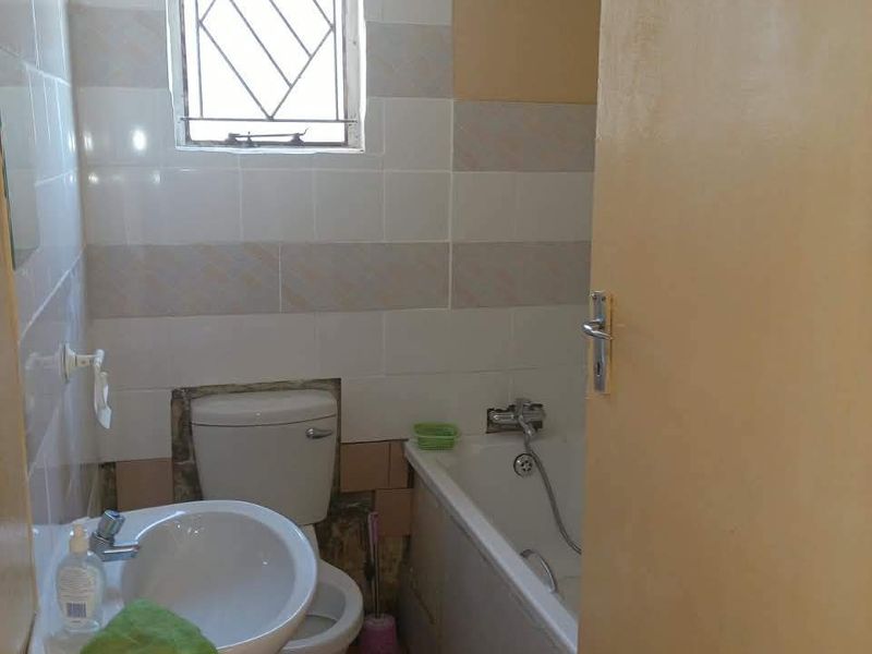 A compact bathroom featuring a pedestal basin, toilet, and bathtub with tiled finishes, currently requiring maintenance and cosmetic updates to the walls and flooring.