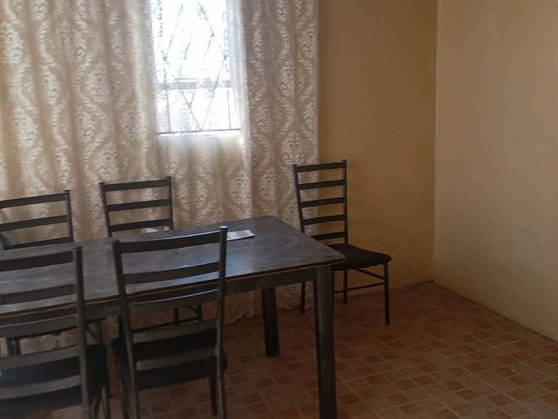 A simple dining area featuring tiled flooring, a window with security bars, and an exposed corrugated metal ceiling.