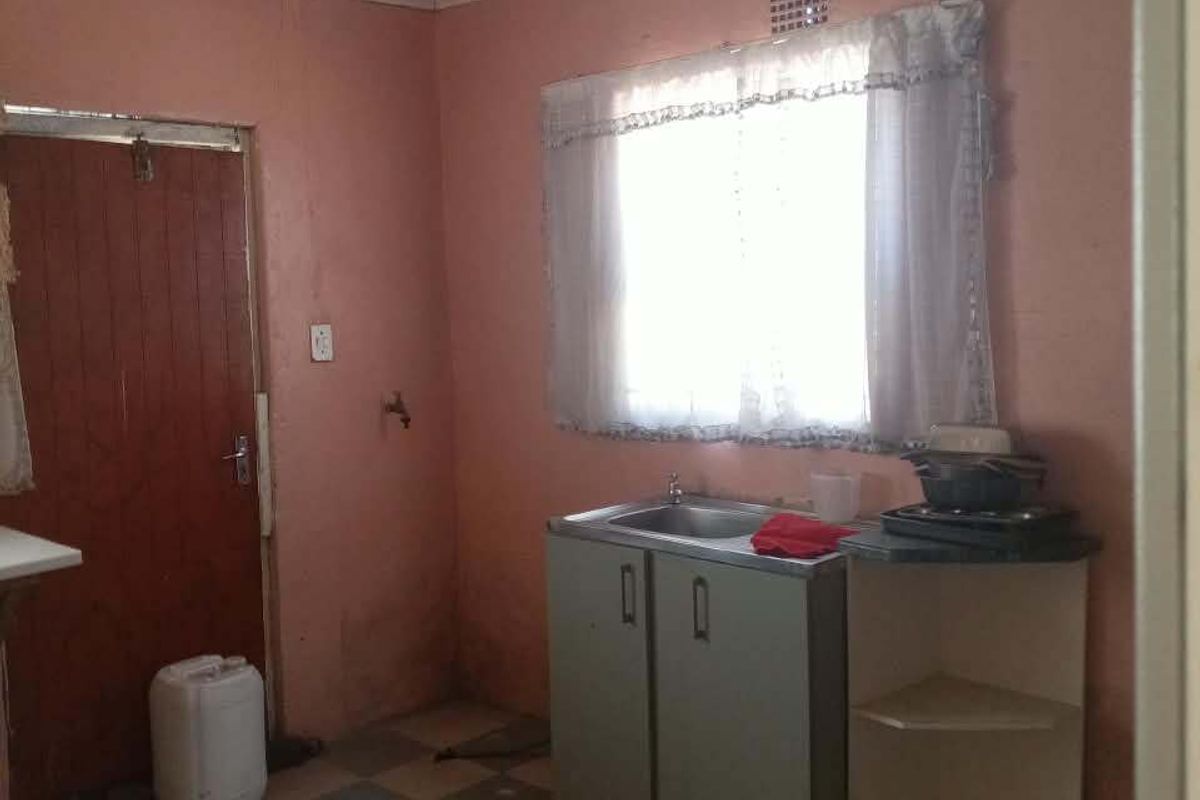A basic kitchen area featuring a sink, built-in cabinetry, and tiled flooring, requiring significant cosmetic updates and repairs to the ceiling and walls.