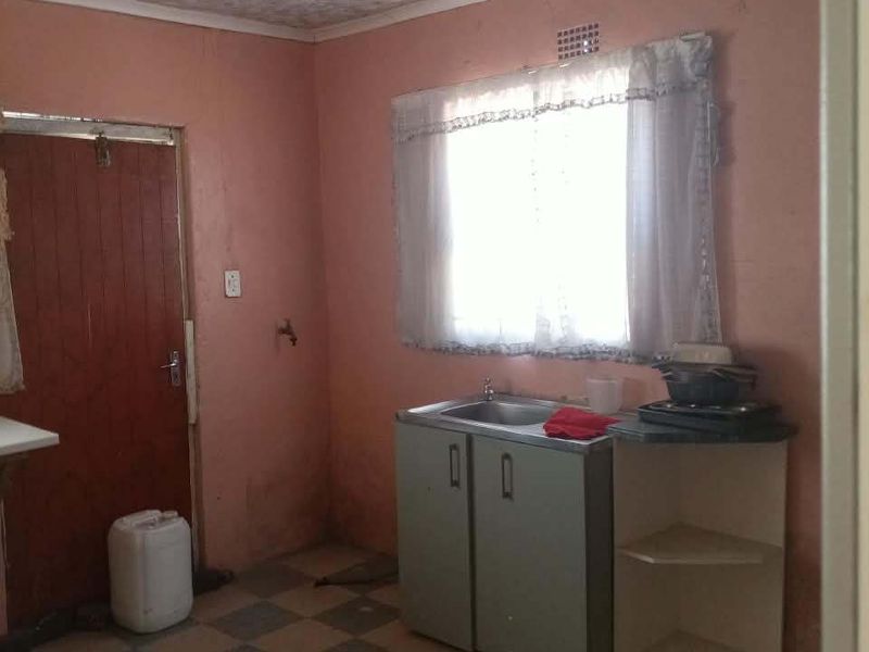 A basic kitchen area featuring a sink, built-in cabinetry, and tiled flooring, requiring significant cosmetic updates and repairs to the ceiling and walls.