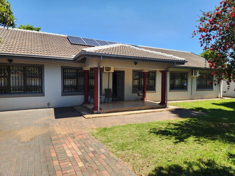 Rear view of a single-story house featuring a covered patio, brick paved driveway, solar panels, and security bars on windows.
