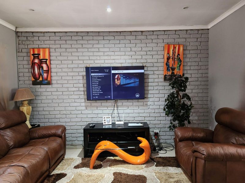 A living room featuring a painted brick accent wall with a wall-mounted television and recessed ceiling lighting.