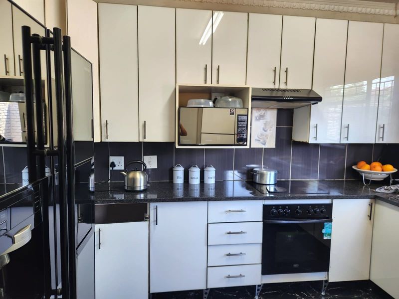 A functional kitchen featuring white cabinetry, dark granite countertops, a tiled backsplash, and integrated appliances including an oven, hob, and extractor fan.