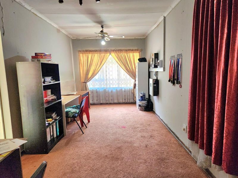 A bedroom featuring carpeted flooring, a ceiling fan, and a security gate over the window. The room requires cosmetic updates to improve its overall condition.