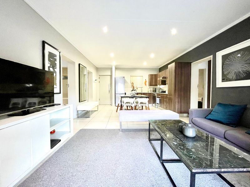 A modern open-plan living and kitchen area featuring tiled floors, recessed lighting, and contemporary dark wood cabinetry with integrated appliances.