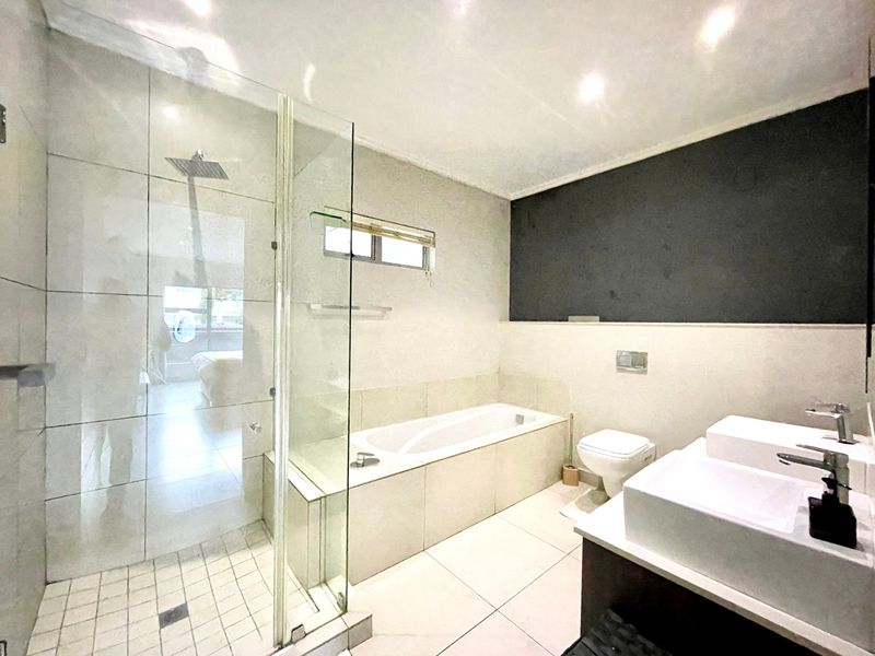 Modern bathroom featuring a glass-enclosed shower, built-in bathtub, wall-mounted toilet, and a double vanity with contemporary fixtures.