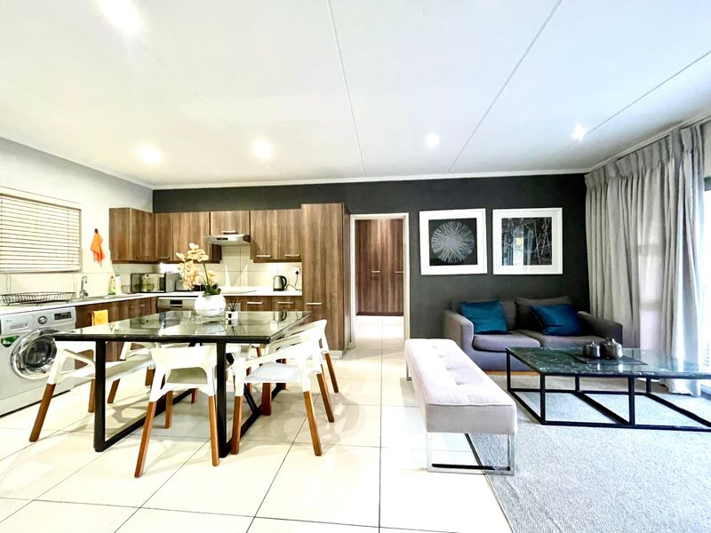 An open-plan living and kitchen area featuring modern wood-finish cabinetry, tiled flooring, and direct access to an outdoor space through sliding doors.