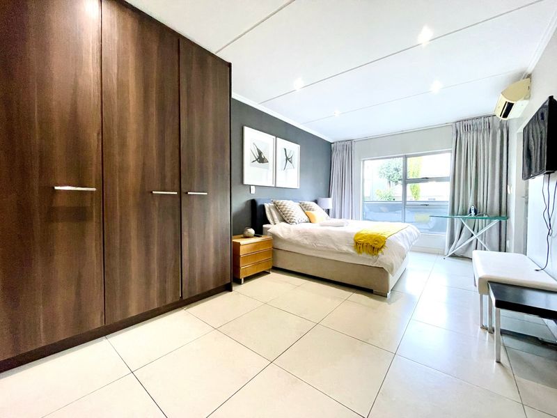 A well-lit bedroom featuring large built-in cupboards, tiled flooring, and a wall-mounted air conditioning unit, offering a clean and functional living space.