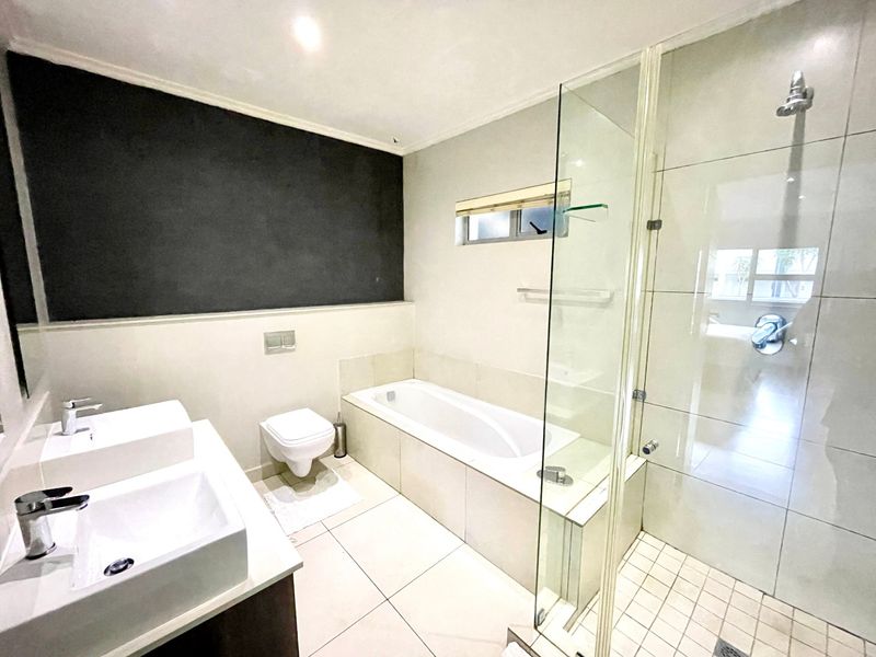 Modern bathroom featuring a double vanity, built-in bathtub, and a separate glass-enclosed shower with tiled finishes.