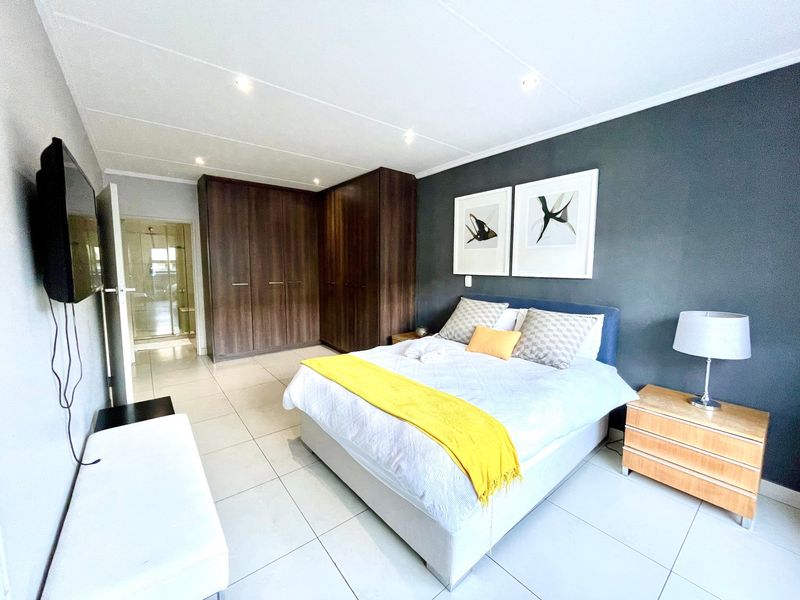 A well-maintained bedroom featuring tiled flooring, built-in wooden cupboards, recessed ceiling lighting, and direct access to an en-suite bathroom.