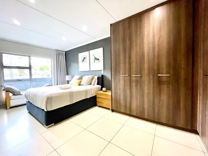 A well-maintained bedroom featuring large built-in cupboards, neutral tiled flooring, and modern recessed lighting, offering a clean and functional living space.