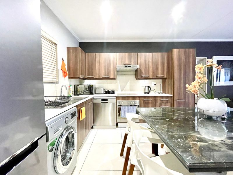 A functional kitchen featuring wood-look cabinetry, stone countertops, integrated appliances, and tiled flooring, providing a practical and well-organized cooking space.