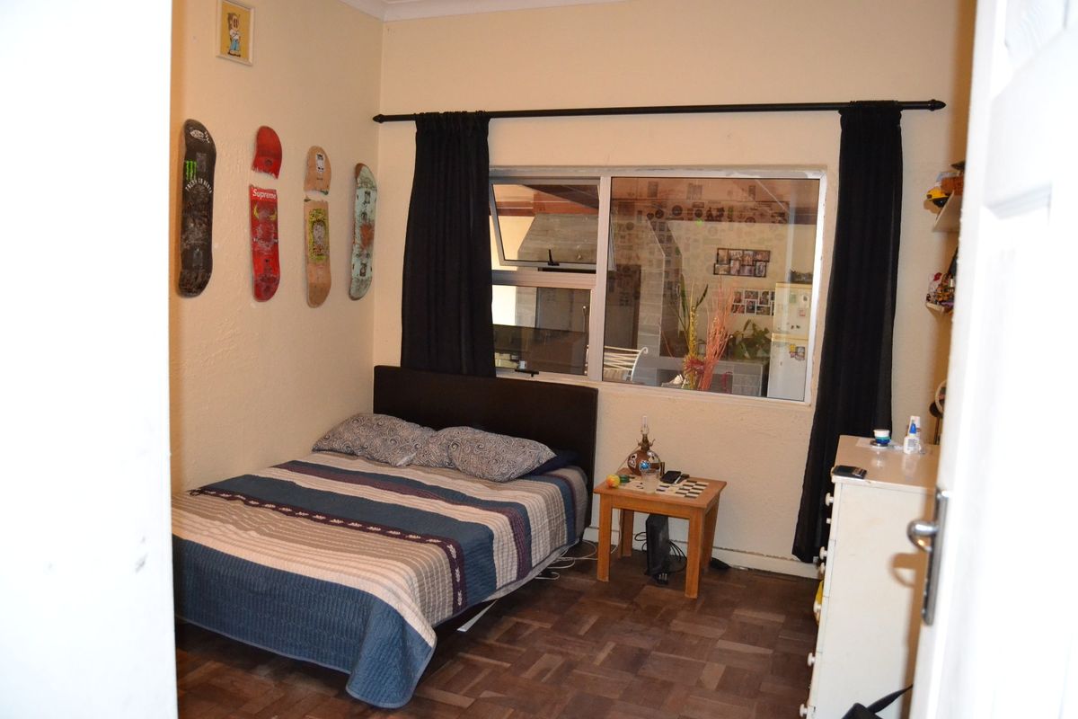 A bedroom featuring parquet flooring and a large window with a curtain rod, offering a functional space with potential for cosmetic updates.