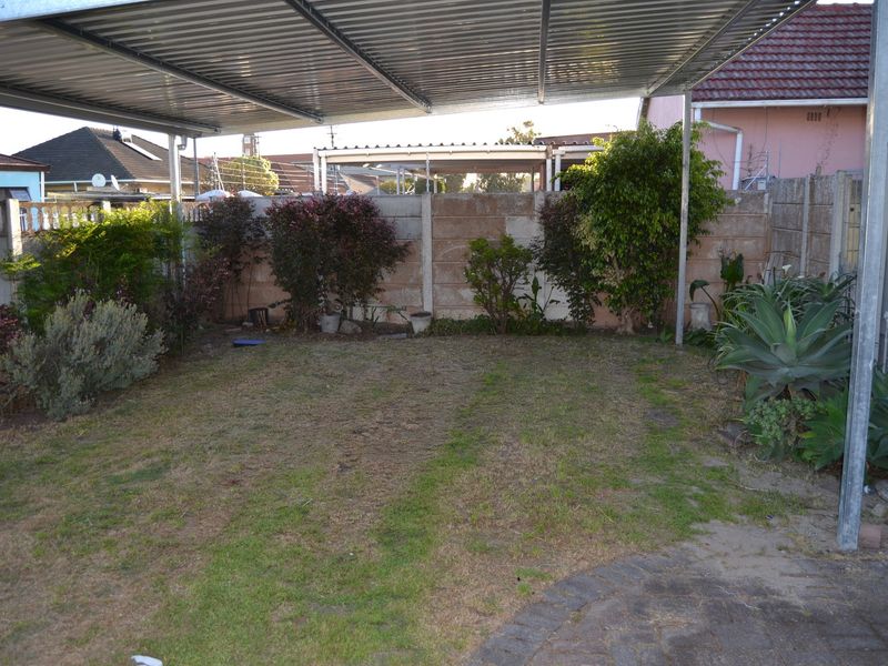 A covered outdoor patio area featuring a corrugated metal roof, paved flooring, and a private garden space enclosed by a precast concrete boundary wall.