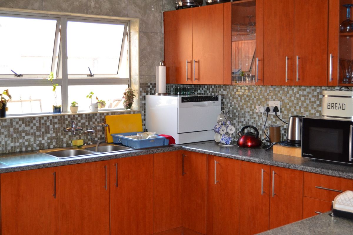 A functional kitchen featuring warm-toned laminate cabinetry, granite countertops, a double bowl stainless steel sink, and a decorative mosaic tile backsplash.