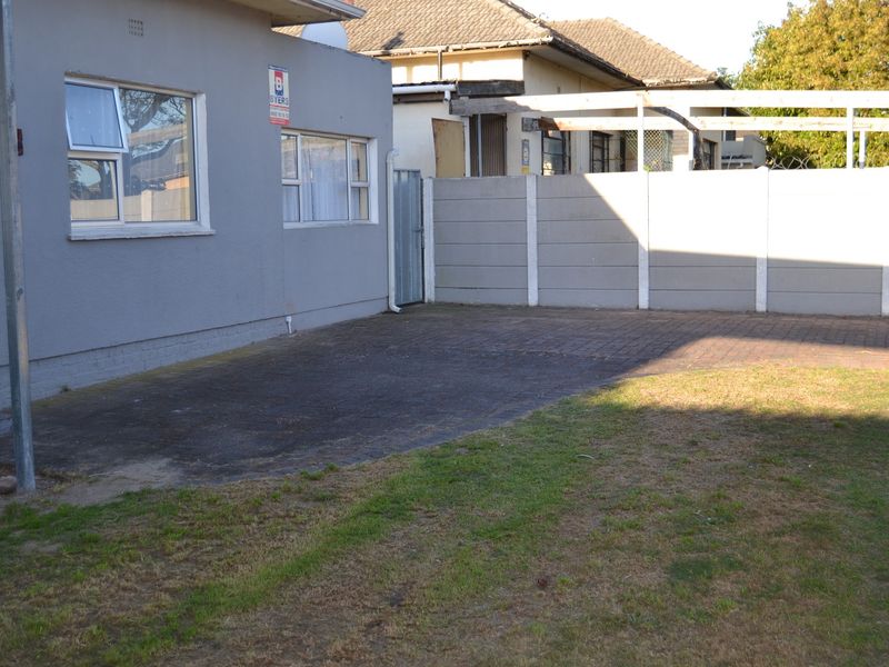 Rear exterior view featuring a paved driveway area, precast concrete boundary wall, and a timber pergola structure.