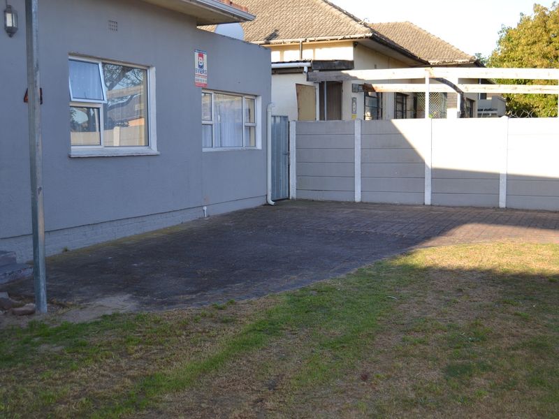 Rear exterior view featuring a paved driveway area, precast concrete boundary wall, and a timber pergola structure in the backyard.