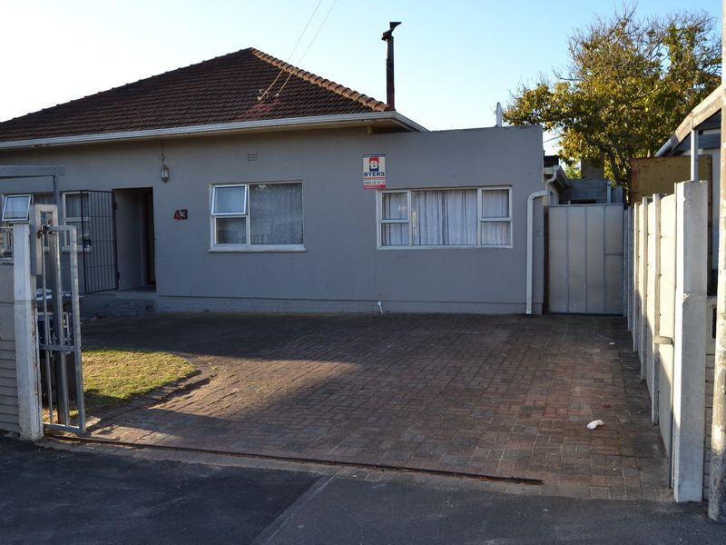 Front elevation of a single-story house featuring a paved driveway, tiled roof, and secure boundary walling.