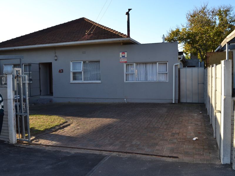 Front elevation of a single-story house featuring a tiled roof, paved driveway, and secure gated entrance with precast boundary walling.