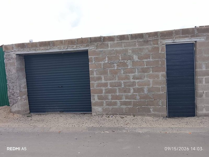 A detached garage structure featuring a roller shutter door and a side access door, currently with unfinished concrete block exterior walls.