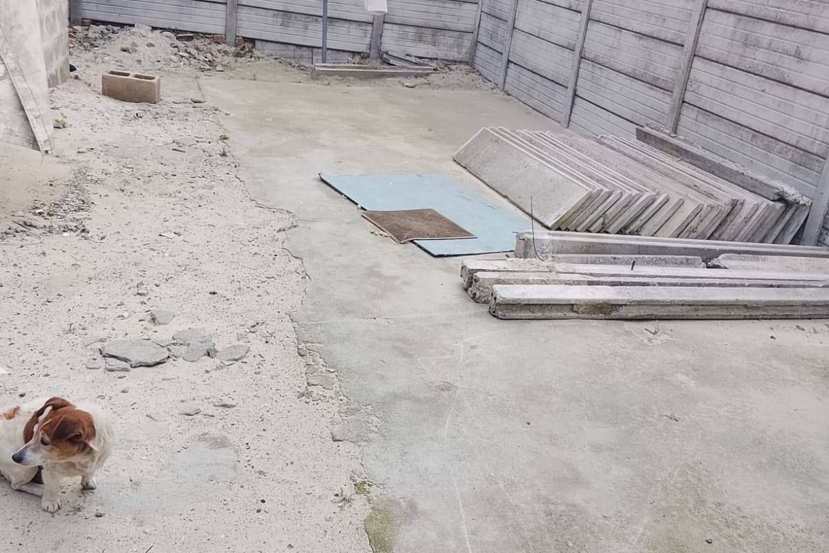 A rear outdoor area featuring precast concrete boundary walls and a concrete slab, currently in an unfinished state with construction materials present.