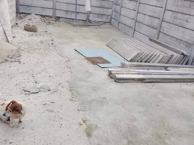 A rear outdoor area featuring precast concrete boundary walls and a concrete slab, currently in an unfinished state with construction materials present.