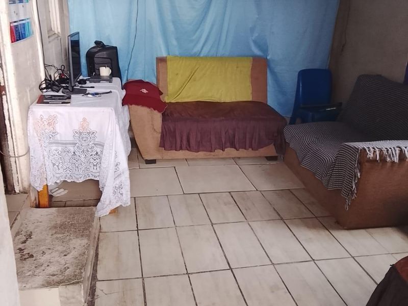 A living area featuring ceramic tiled flooring and a wall-mounted air conditioning unit, currently requiring cosmetic updates and wall finishing.