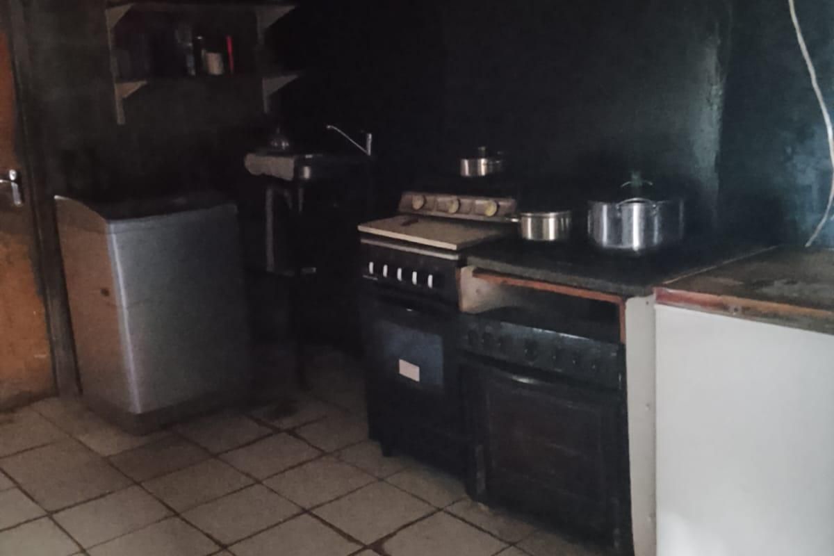 A basic kitchen area featuring a built-in stove, oven, sink, and tiled flooring, requiring significant renovation and improved lighting to modernize the space.