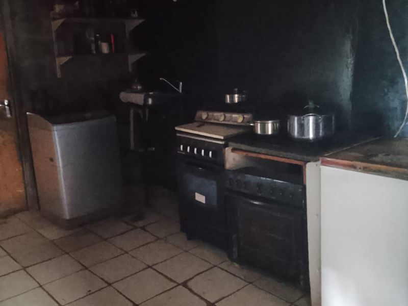 A basic kitchen area featuring a built-in stove, oven, sink, and tiled flooring, requiring significant renovation and improved lighting to modernize the space.