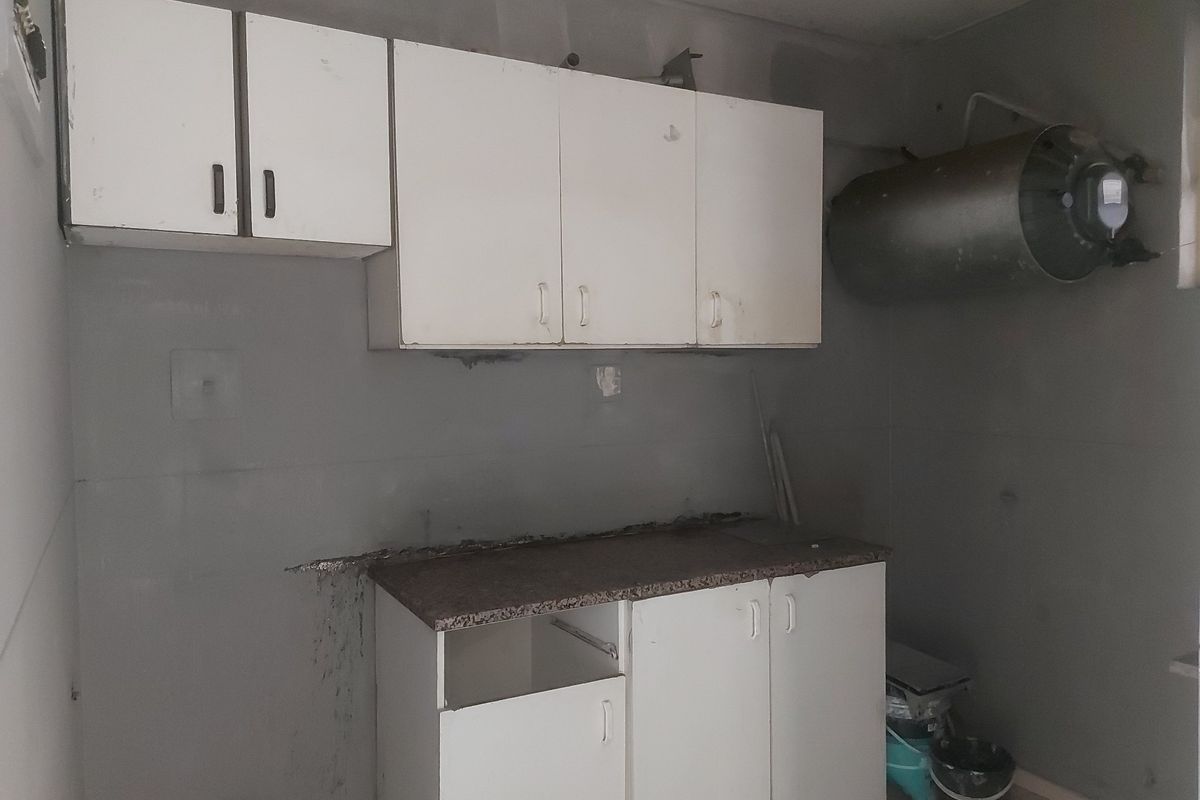 A dated kitchen area featuring basic cabinetry and an exposed water heater, requiring significant renovation and cosmetic updates to improve functionality and aesthetic appeal.