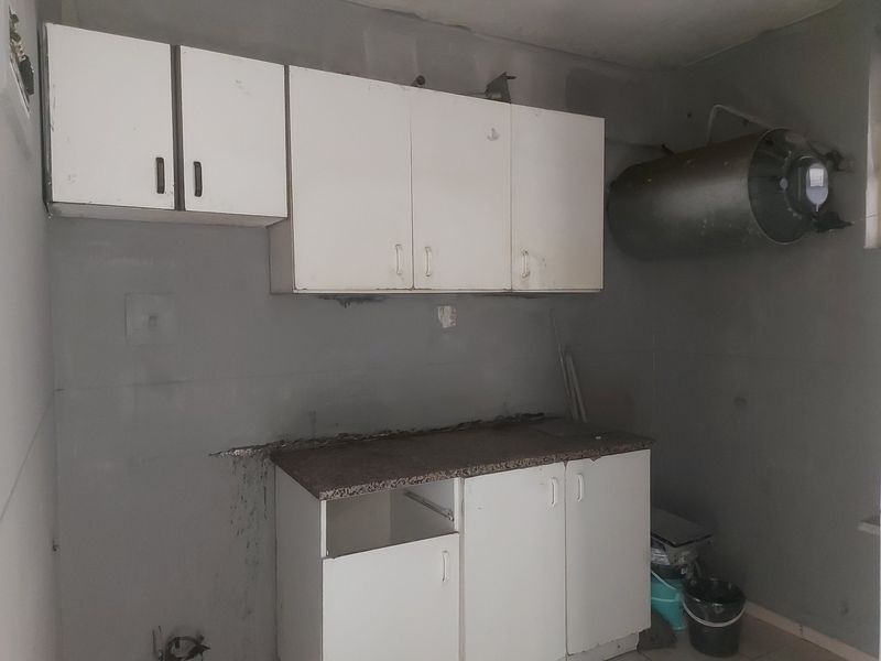 A dated kitchen area featuring basic cabinetry and an exposed water heater, requiring significant renovation and cosmetic updates to improve functionality and aesthetic appeal.