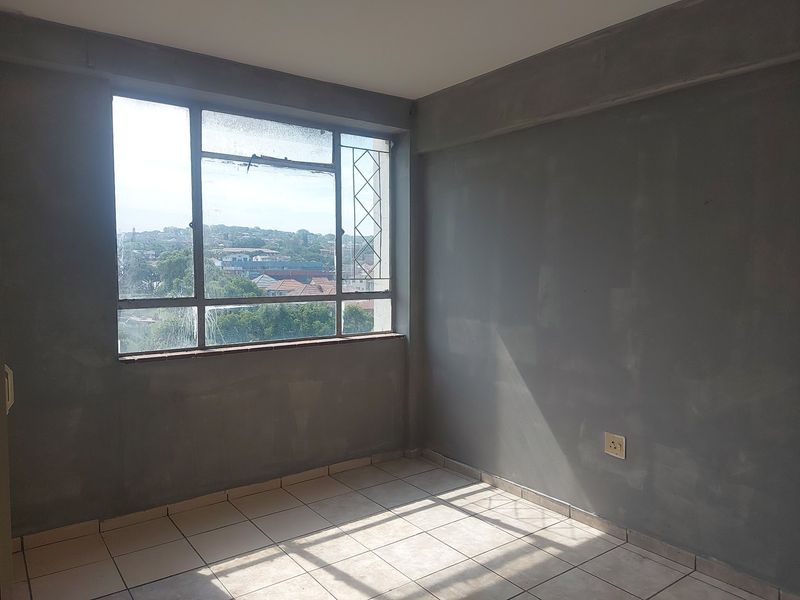 An empty bedroom featuring tiled flooring and large windows with views, currently requiring wall finishing and general maintenance to reach its full potential.