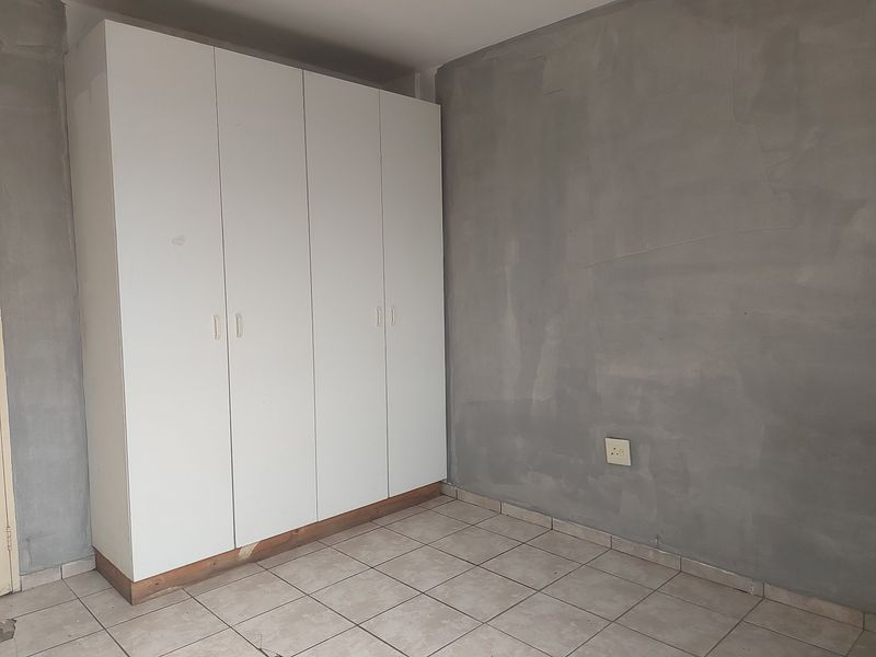 A bedroom featuring tiled flooring and a built-in wardrobe, currently requiring wall finishing and cosmetic repairs to the cabinetry base.