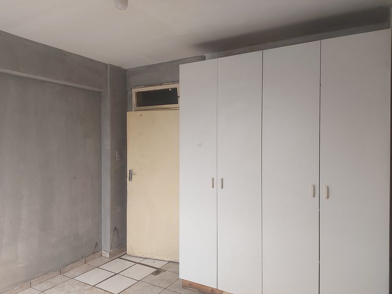 An empty bedroom featuring built-in cupboards, tiled flooring, and unfinished wall surfaces, offering a blank canvas for renovation and personalization.