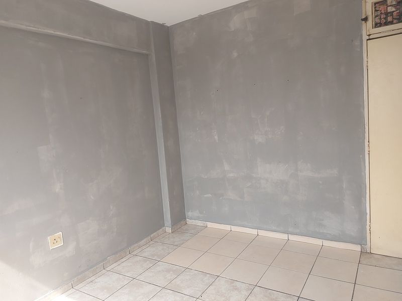 An empty bedroom featuring ceramic floor tiles and walls requiring finishing or painting, offering a blank canvas for renovation.