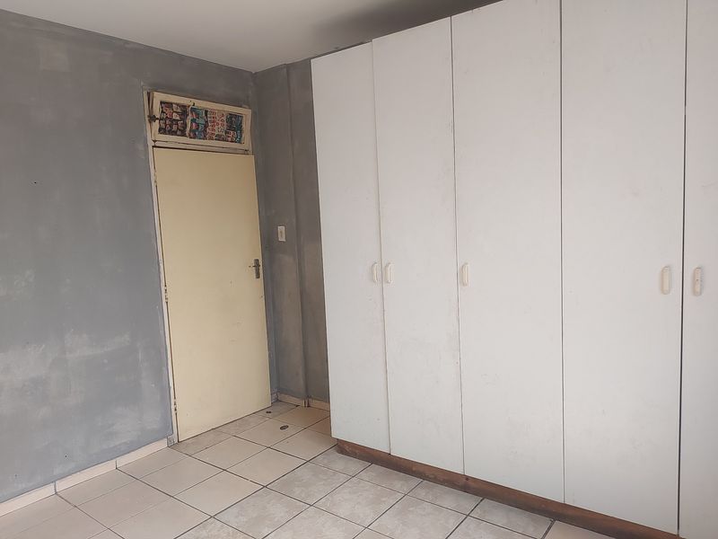 A bedroom featuring built-in cupboards and tiled flooring, currently requiring cosmetic updates and finishing to the wall surfaces.